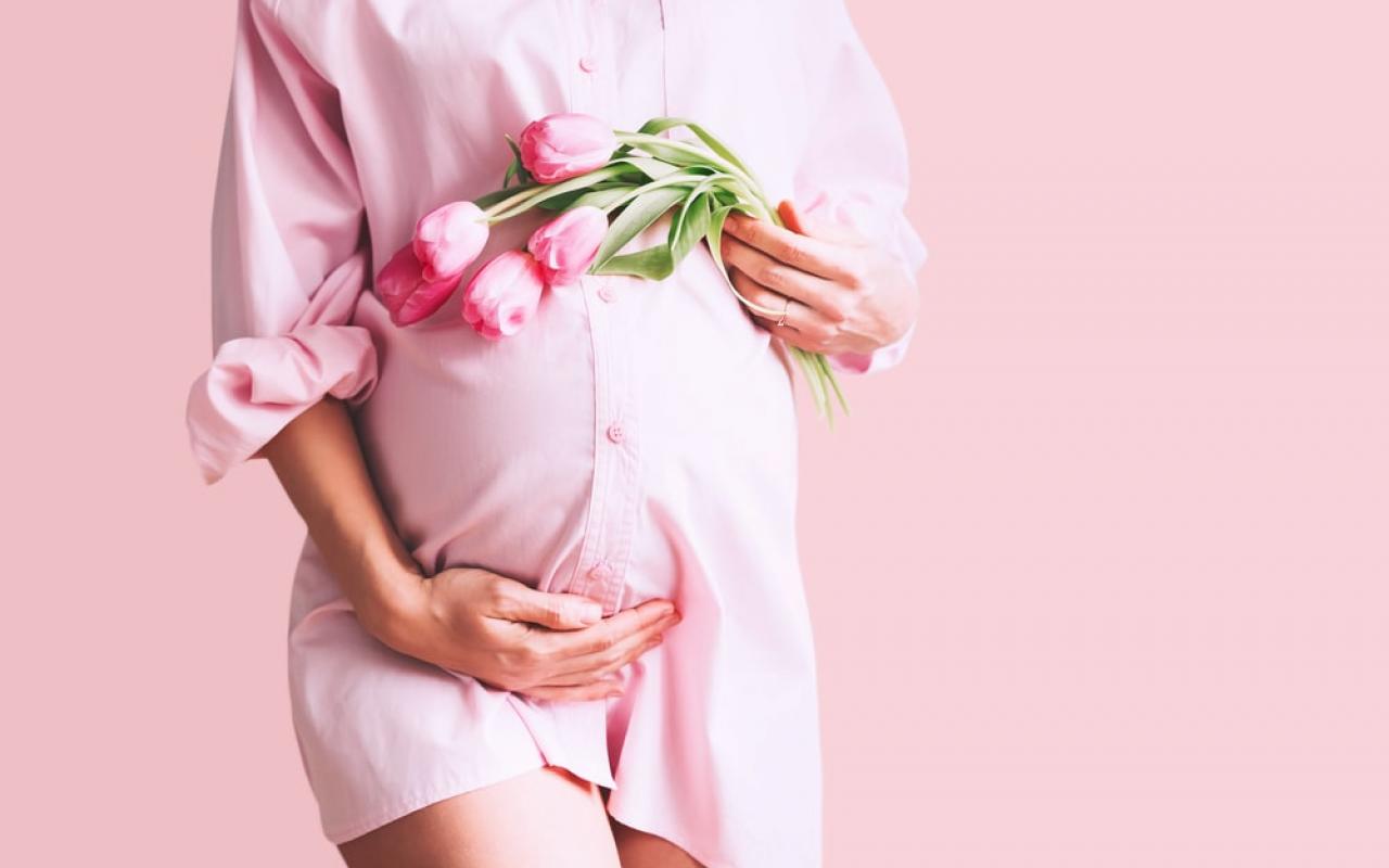 Giovane donna in abito camicia premaman con fiori di tulipani tiene le mani sulla pancia