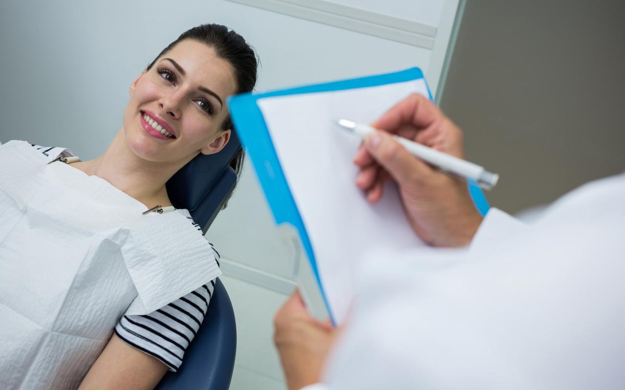 doctor-writing-on-clipboard-while-patient-lying-on-dental-bed