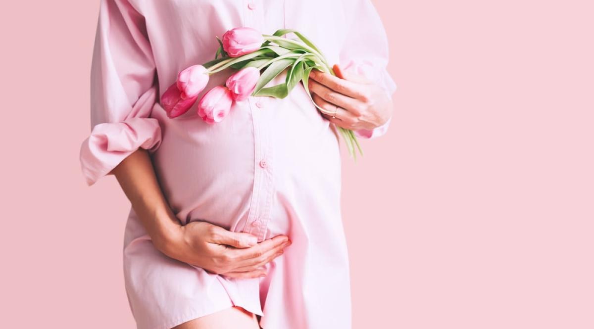 Giovane donna in abito camicia premaman con fiori di tulipani tiene le mani sulla pancia