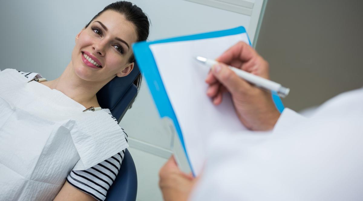 doctor-writing-on-clipboard-while-patient-lying-on-dental-bed